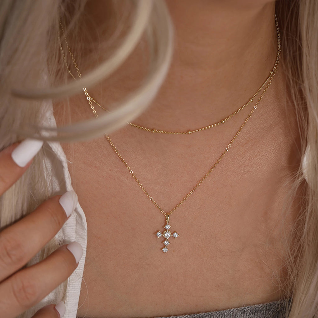Close view of a gold-tone cross necklace worn on the neck with clear stones