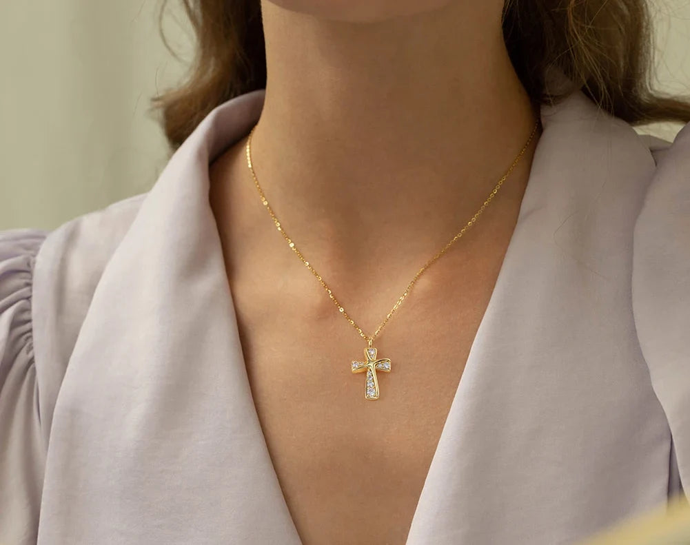 Gold-tone curved cross necklace with clear CZ stones worn at the base of the neck