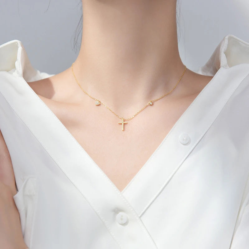 Gold-tone cross necklace worn at the base of the neck with heart and star charms