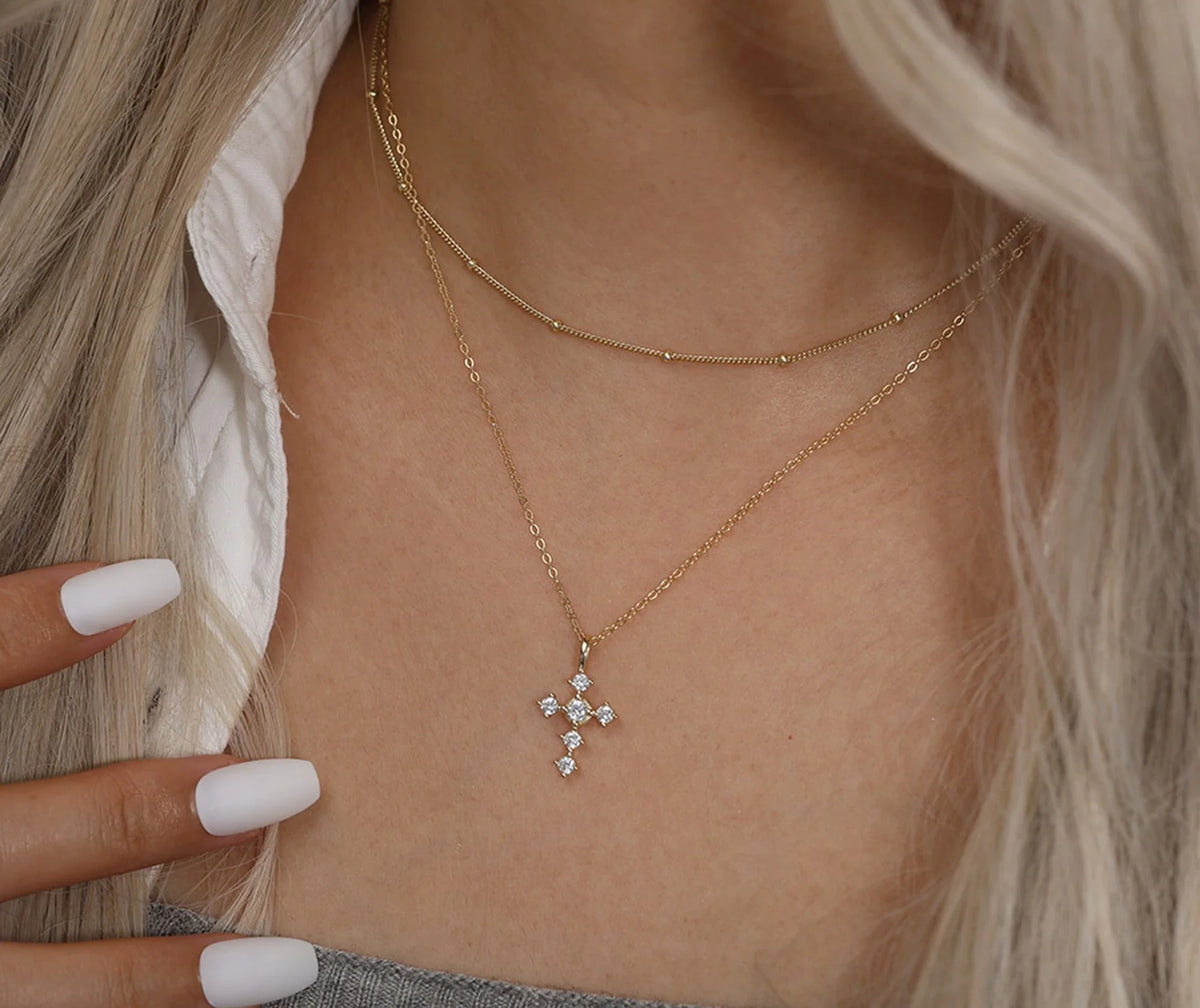 Gold-tone stone-set cross necklace worn at the base of the neck