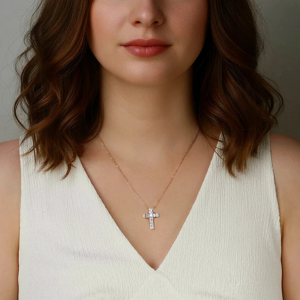 Gold-tone moissanite cross necklace worn over a white V-neck top, centered below the collarbone