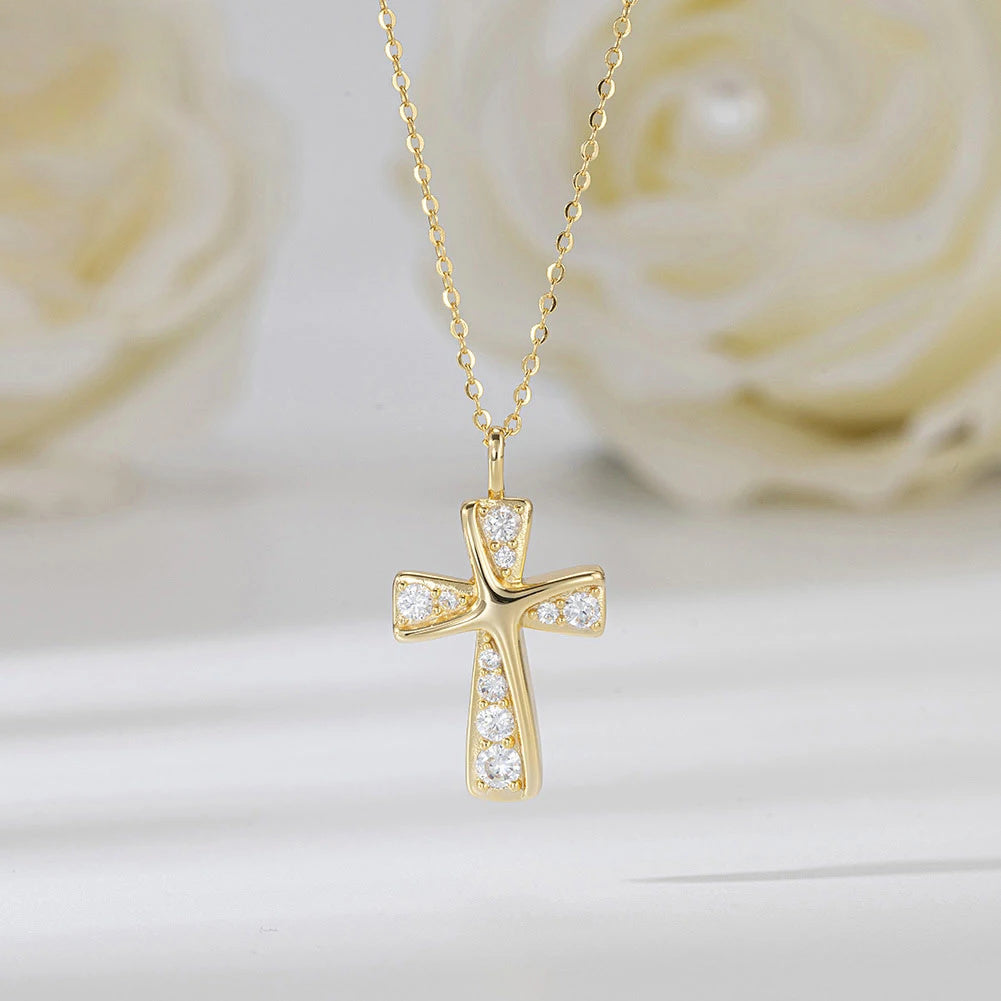Gold-tone curved cross pendant with clear CZ stones suspended before pale flowers