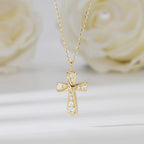 Gold-tone curved cross pendant with clear CZ stones suspended before pale flowers