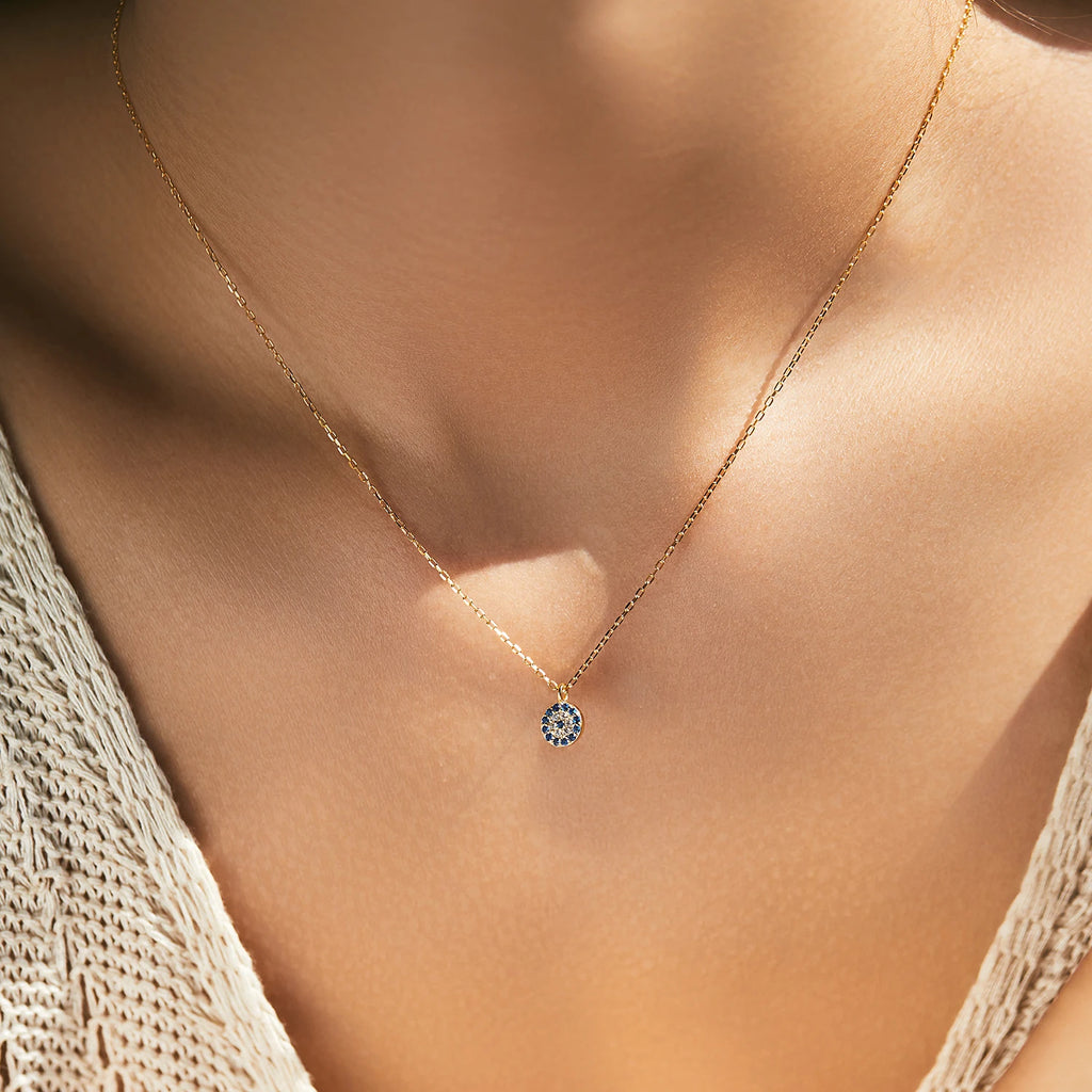 Gold-tone evil eye pendant necklace worn at the base of the neck with blue and clear stones
