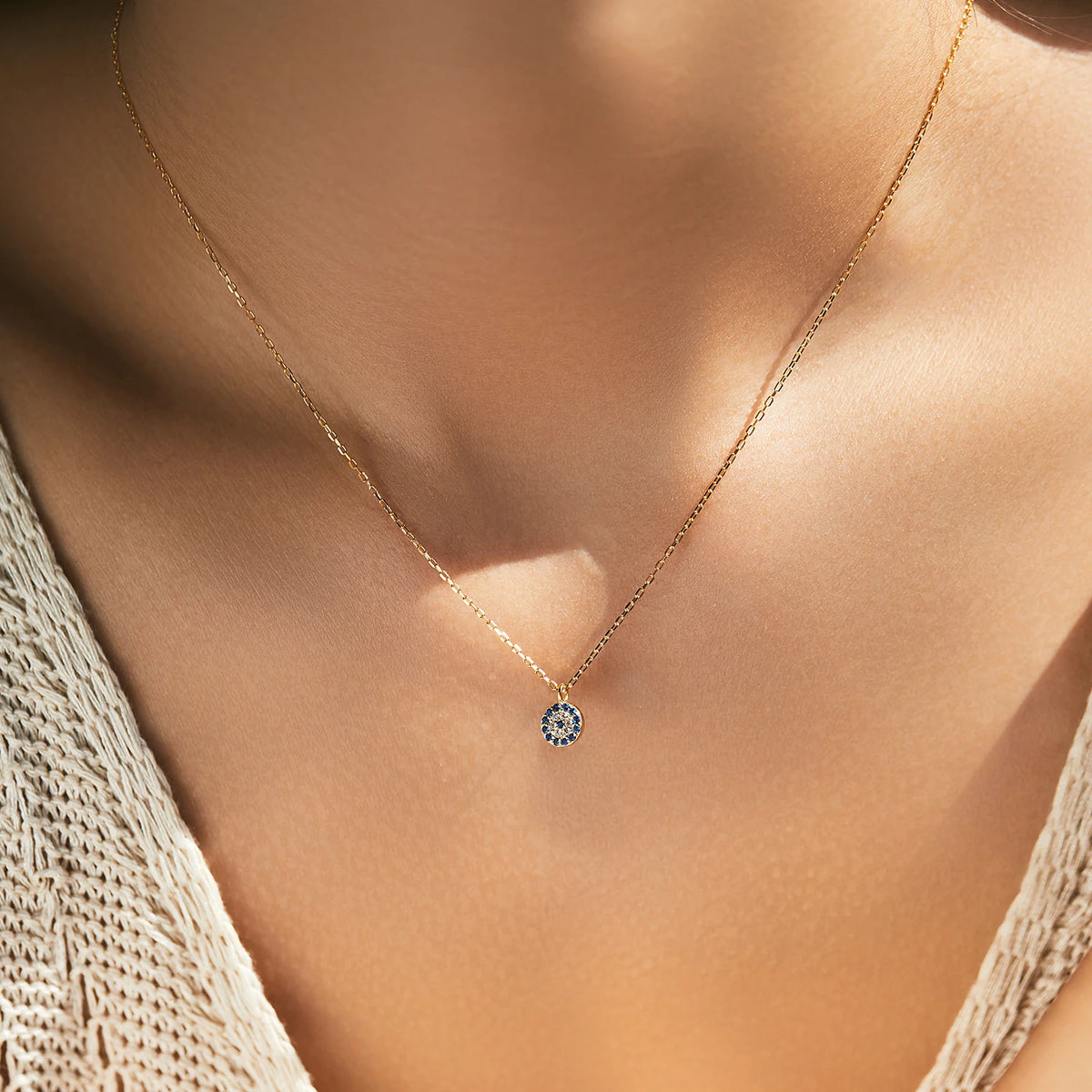 Gold-tone evil eye pendant necklace worn at the base of the neck with blue and clear stones