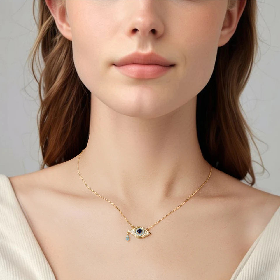 Gold-tone evil eye necklace worn with an off-white top, showing the small blue stone-set pendant at the collarbone