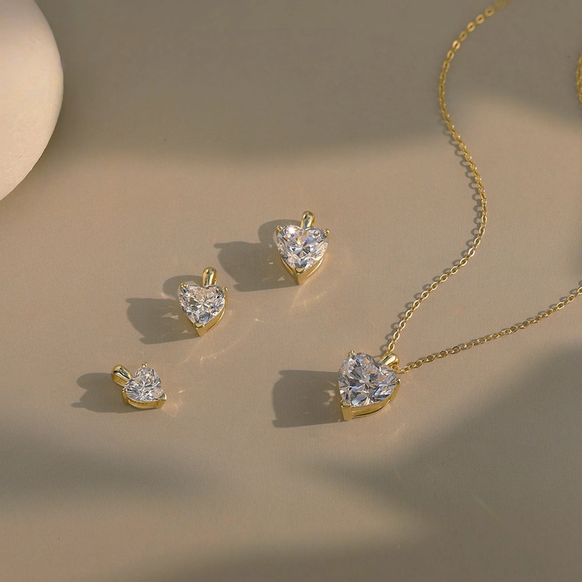 Gold-tone heart pendants in several sizes beside a matching clear heart necklace on a neutral surface