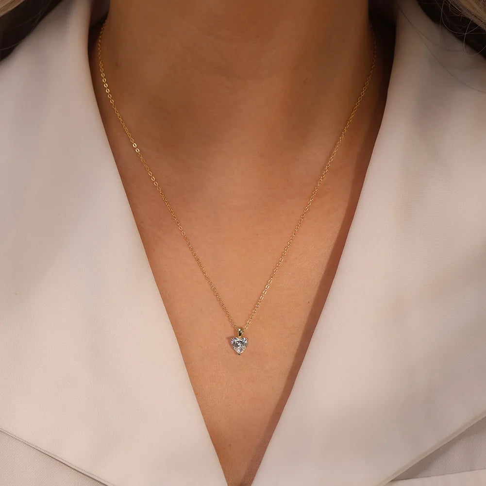 Gold-tone heart moissanite necklace worn at the collarbone with a white V-neck blouse