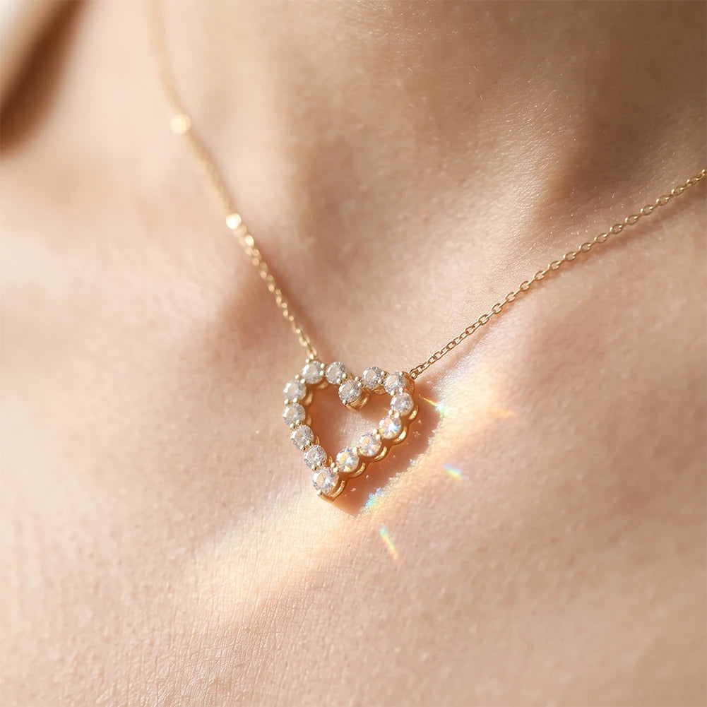 Gold-tone hollow heart necklace worn at the base of the throat with sparkling round stones