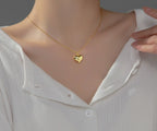 Polished gold heart necklace worn at the neckline with a puffed mirror-finish pendant