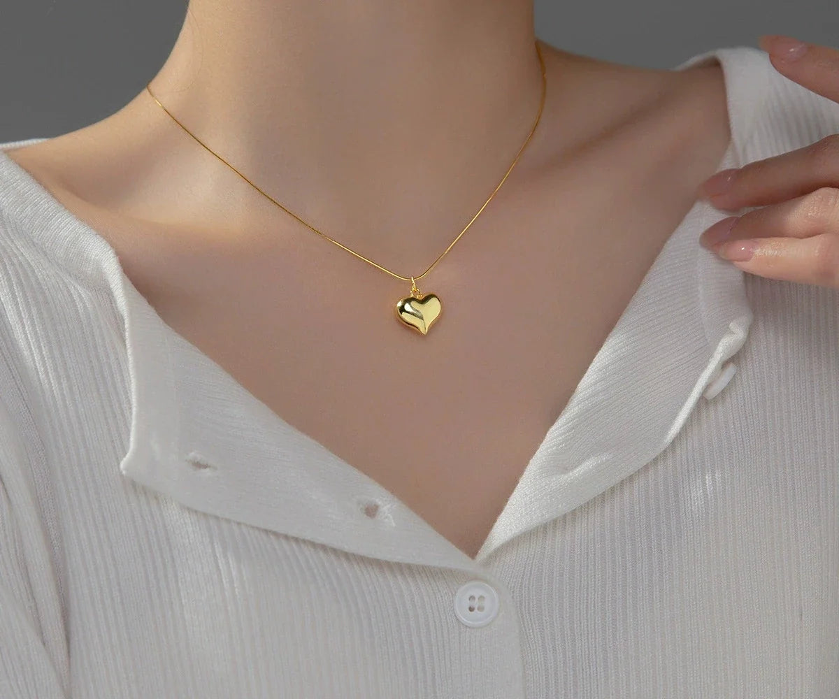 Polished gold heart necklace worn at the neckline with a puffed mirror-finish pendant