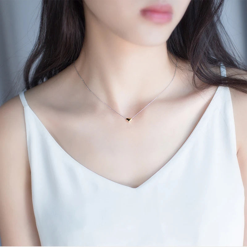 Small gold-colored heart necklace worn at the neckline with a fine silver-tone chain