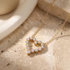 Angled view of a gold-tone hollow heart pendant with round stones and heart-shaped point