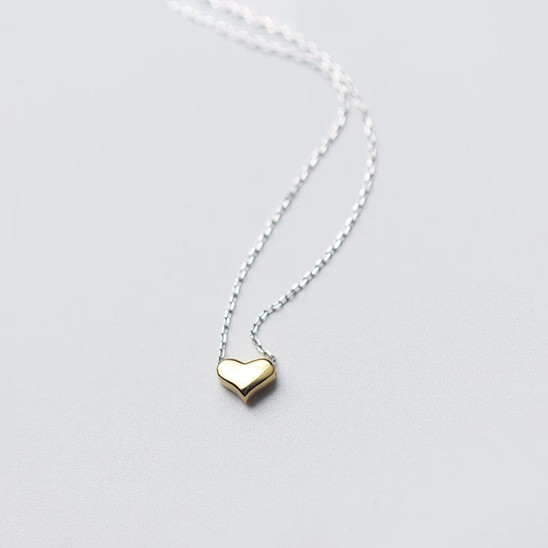 Close-up of a rounded gold-colored heart pendant threaded onto a silver-tone link chain
