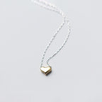 Close-up of a rounded gold-colored heart pendant threaded onto a silver-tone link chain