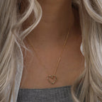 Gold-tone open heart necklace worn on the chest above a gray ribbed top