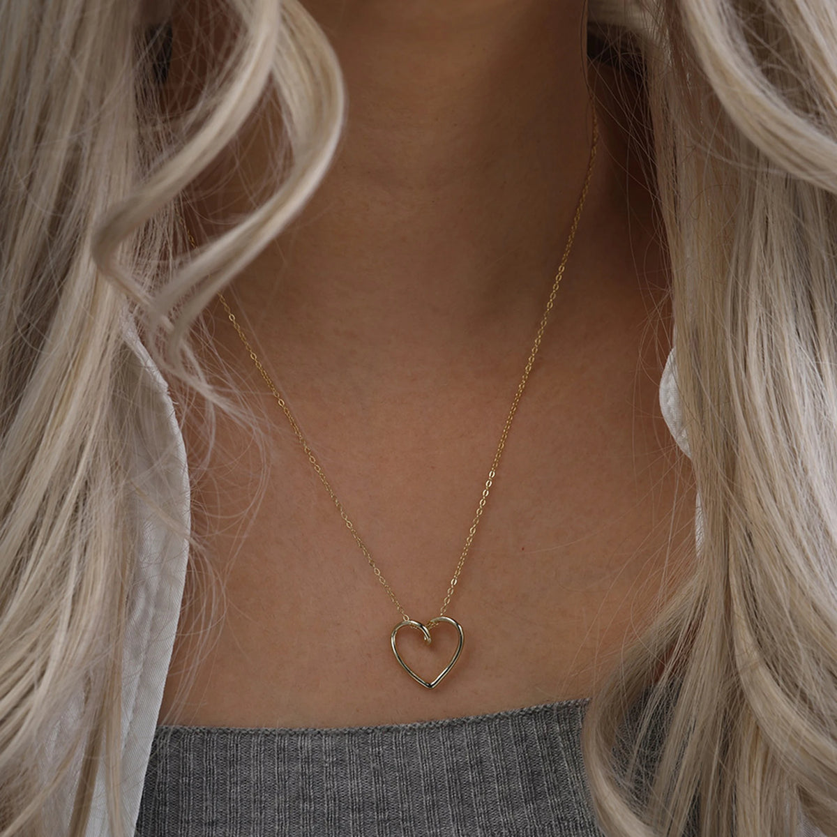Gold-tone open heart necklace worn on the chest above a gray ribbed top