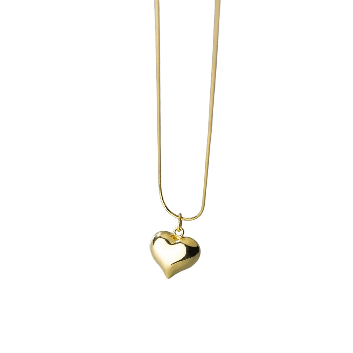 Gold-tone puffed heart pendant hanging from a slim smooth chain on a white background