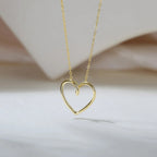 Twisted open heart necklace in a gold-tone finish suspended over a softly draped neutral backdrop