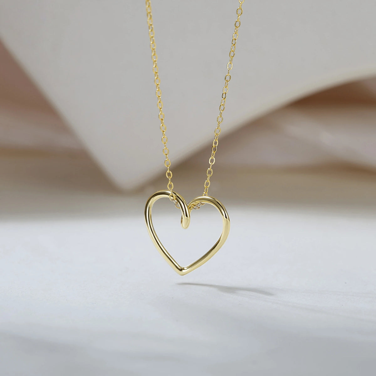 Twisted open heart necklace in a gold-tone finish suspended over a softly draped neutral backdrop