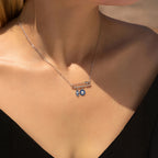 Sterling silver safety pin necklace worn at the collarbone with blue Hamsa and evil eye charms