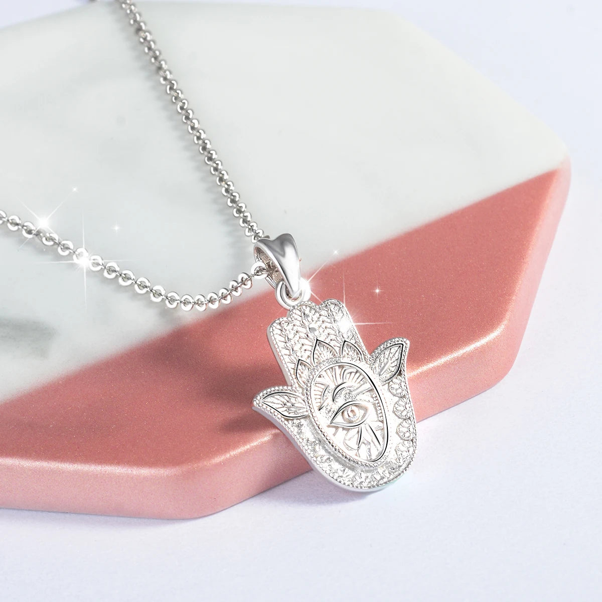 Silver hamsa pendant necklace draped over pink and white display blocks with a raised eye center