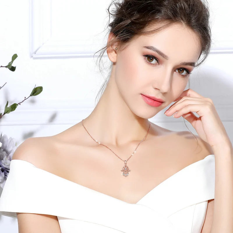 Rose gold-colored hamsa evil eye necklace worn at the base of the neck with an off-shoulder white top
