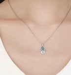 Silver-tone hamsa necklace worn with a white top, featuring a blue stone circle and star at the palm