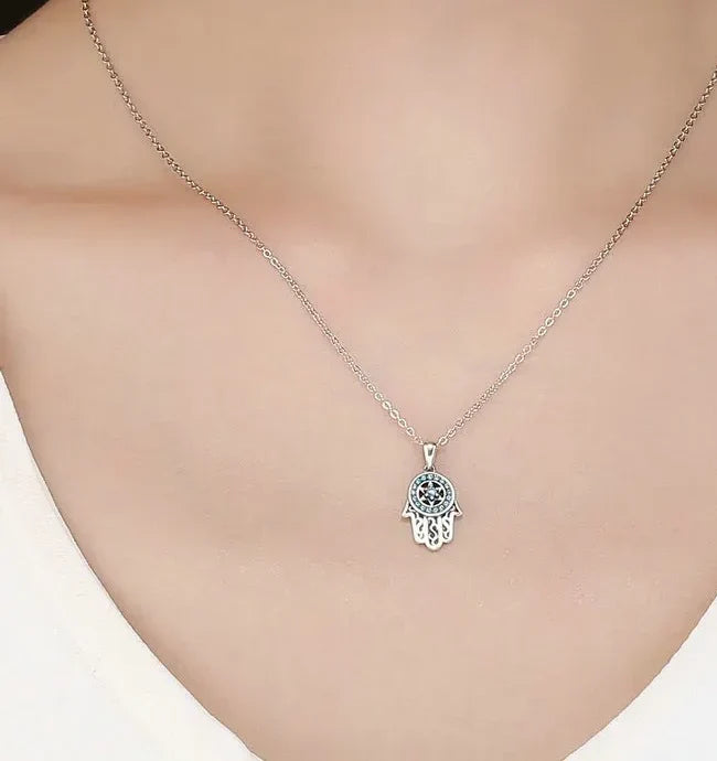 Silver-tone hamsa necklace worn with a white top, featuring a blue stone circle and star at the palm