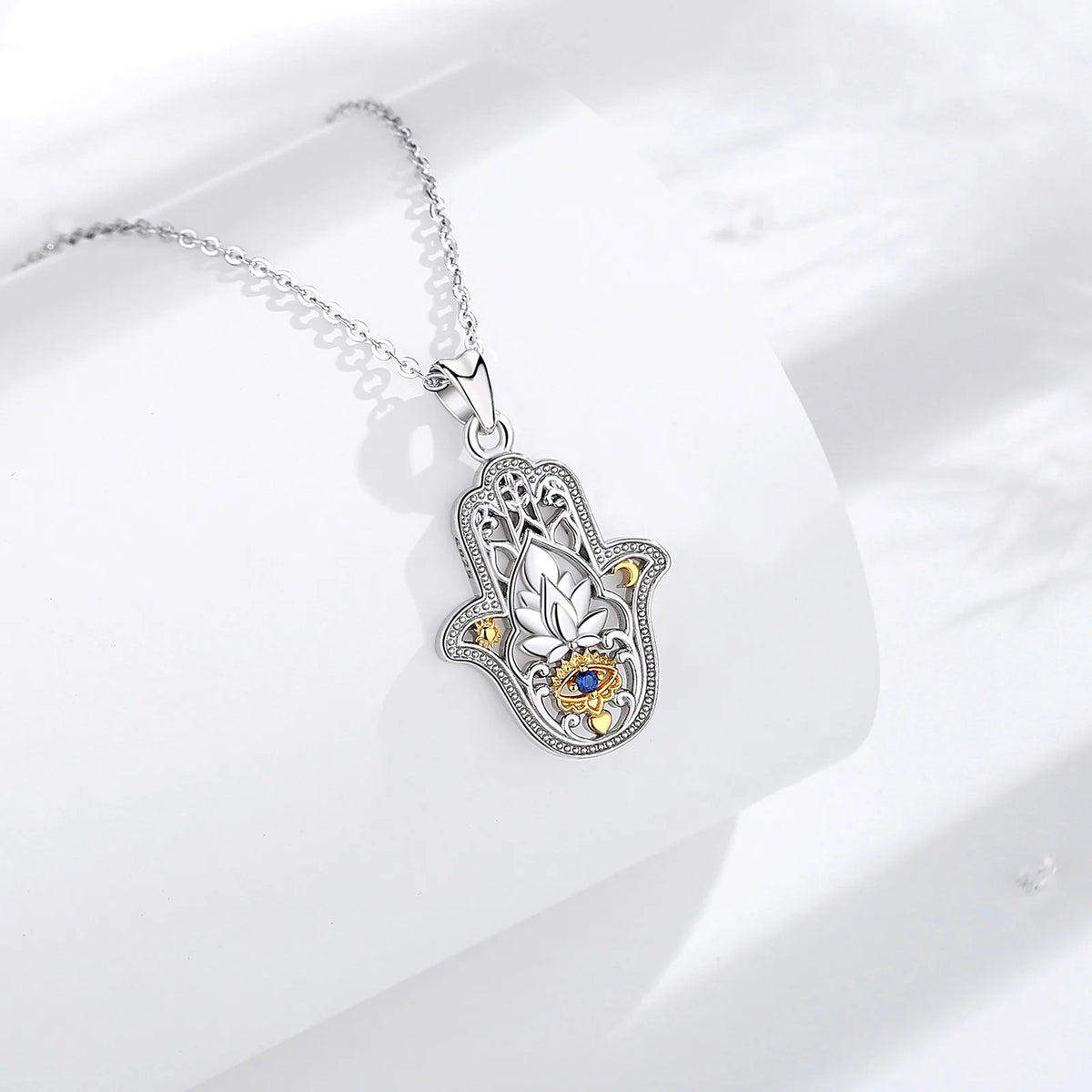 Detailed hamsa pendant necklace on a white display block, showing the lotus and blue eye centerpiece