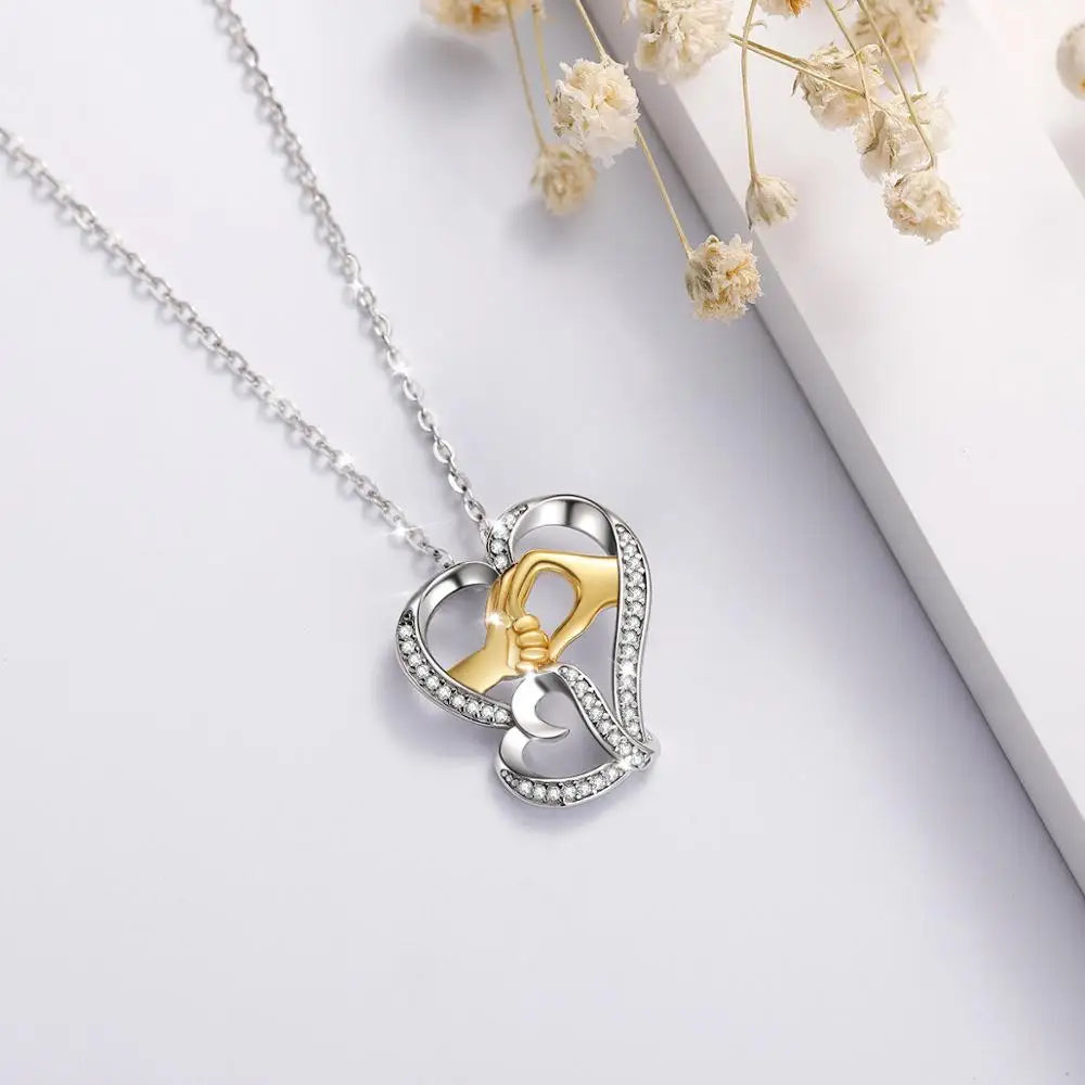 Two-tone heart necklace arranged on a pale surface beside dried flowers and a white display block