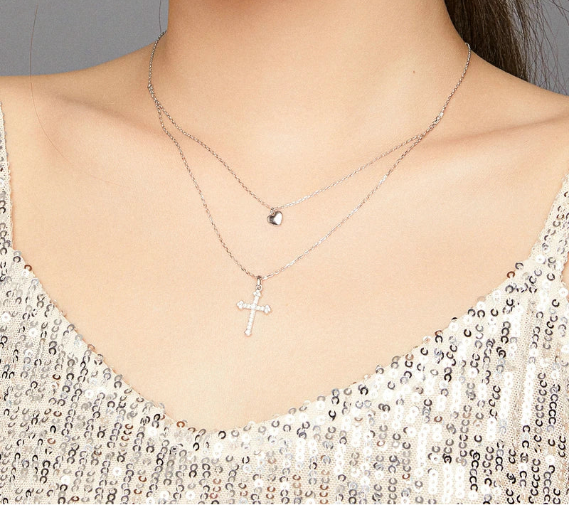 Two-chain sterling silver necklace worn on the neck with a heart pendant above a stone-set cross