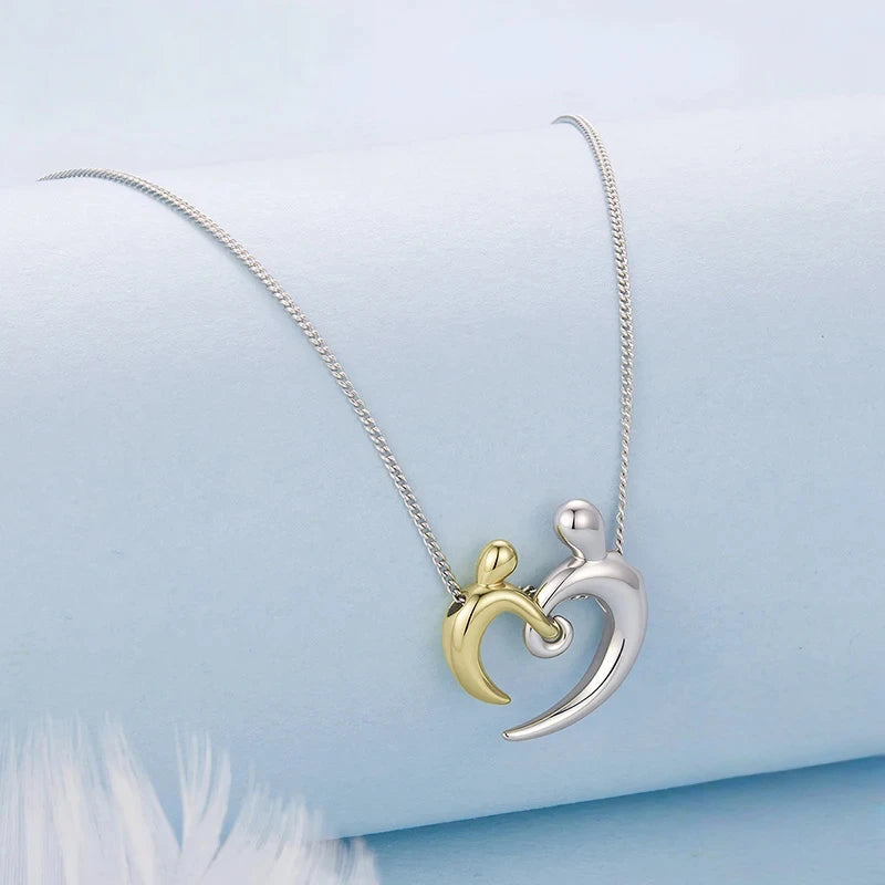 Two-tone heart embrace pendant on a silver-colored chain arranged on a pale blue surface