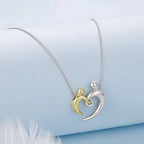 Two-tone heart embrace pendant on a silver-colored chain arranged on a pale blue surface