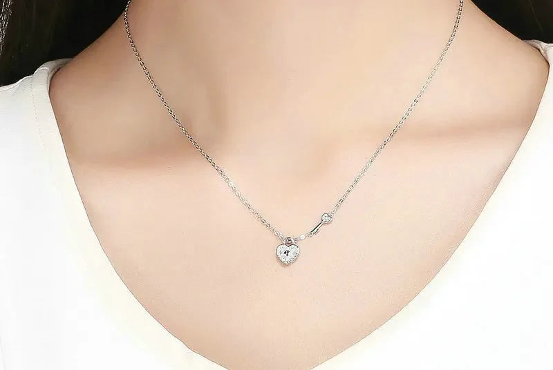 Small heart lock and key necklace worn at the base of the neck on a silver cable chain
