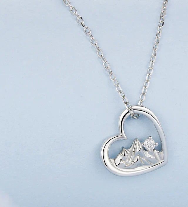 Close-up of the polished heart necklace with sculpted peaks and clear cubic zirconia stone on pale blue