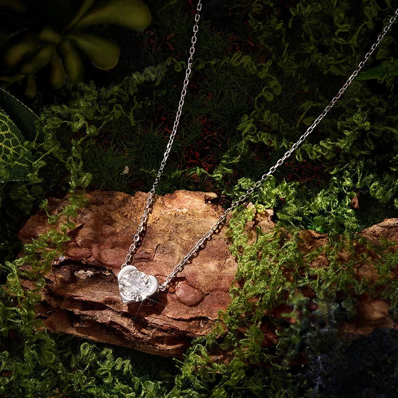 Silver-tone heart necklace with a faceted moissanite displayed on bark and moss