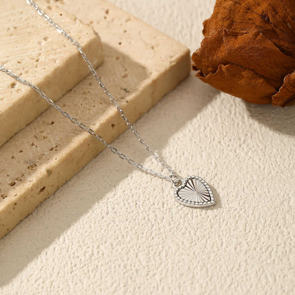 Sterling silver heart necklace on a textured surface beside stone blocks and a dried leaf