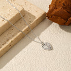 Sterling silver heart necklace on a textured surface beside stone blocks and a dried leaf