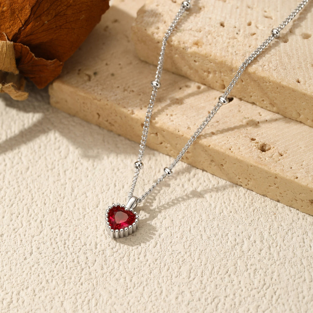 Silver-tone heart necklace laid across stone blocks with a faceted deep red center stone