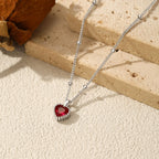 Silver-tone heart necklace laid across stone blocks with a faceted deep red center stone