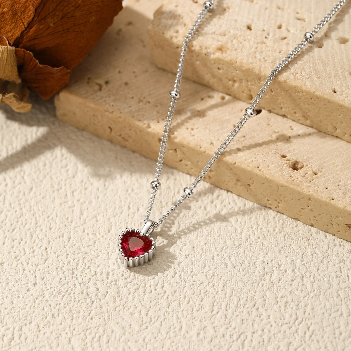 Silver-tone heart necklace laid across stone blocks with a faceted deep red center stone