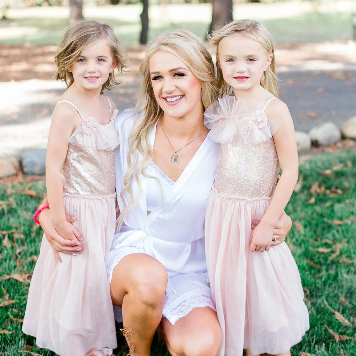 Woman wearing a small silver heart necklace while posing outdoors with two young children