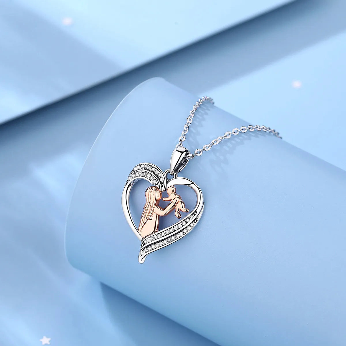 Silver-colored heart pendant with rose-gold-colored mother and baby on a blue display block