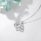 Polished sterling silver heart and infinity necklace arranged on a white surface beside pale petals