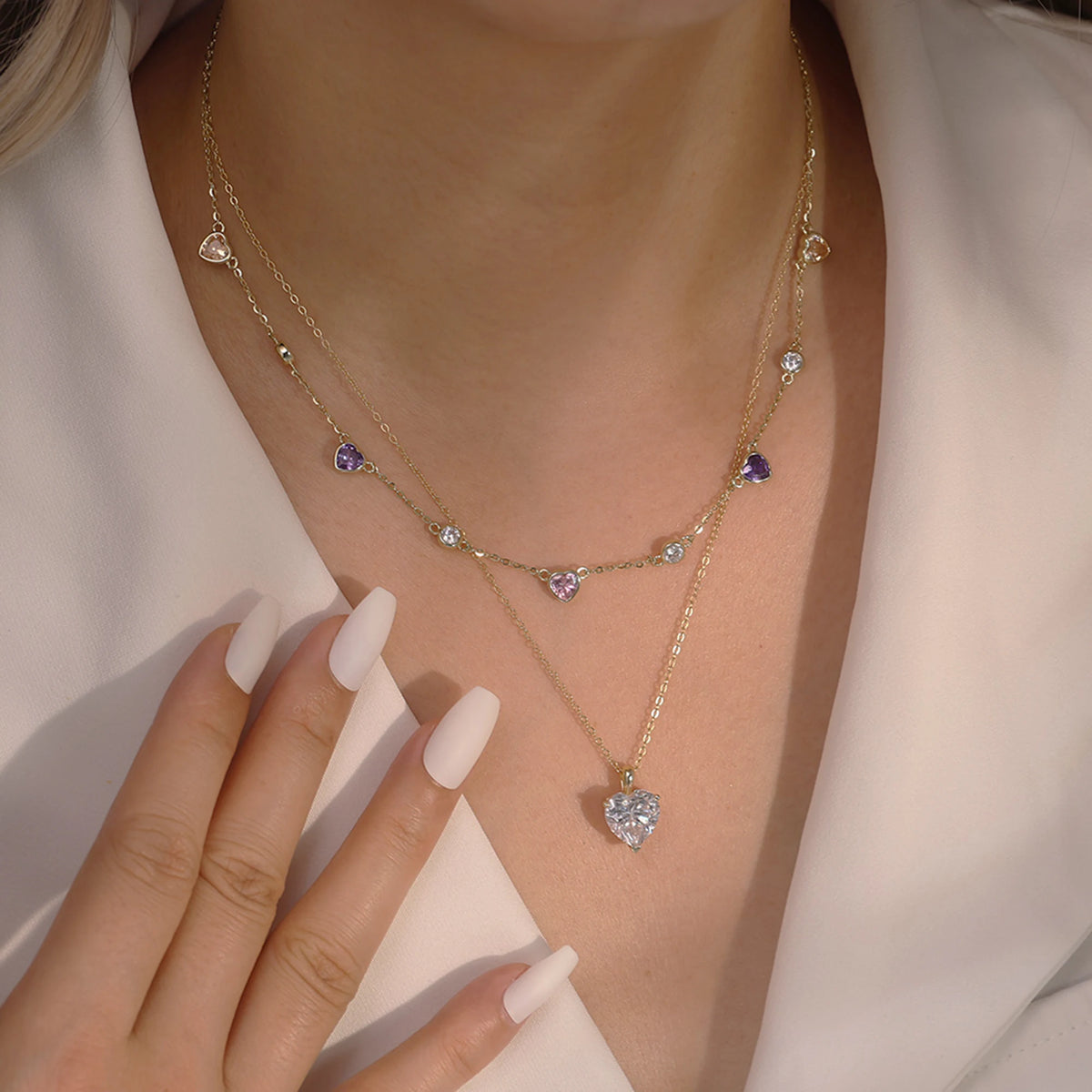 Largest gold-tone clear heart necklace worn below the collarbone against a white neckline