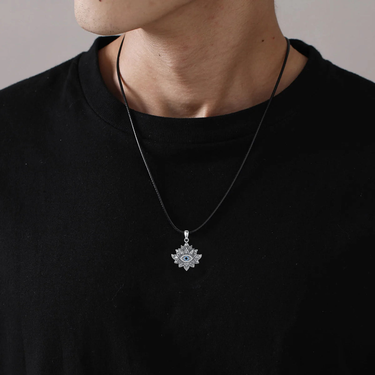 Lotus evil eye pendant worn on a black cord over a black crewneck shirt