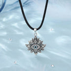 Lotus evil eye necklace hanging from a black braided rope over a pale blue background with clear stones