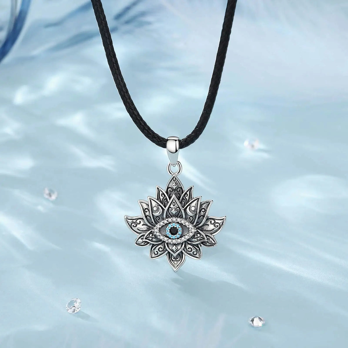 Lotus evil eye necklace hanging from a black braided rope over a pale blue background with clear stones