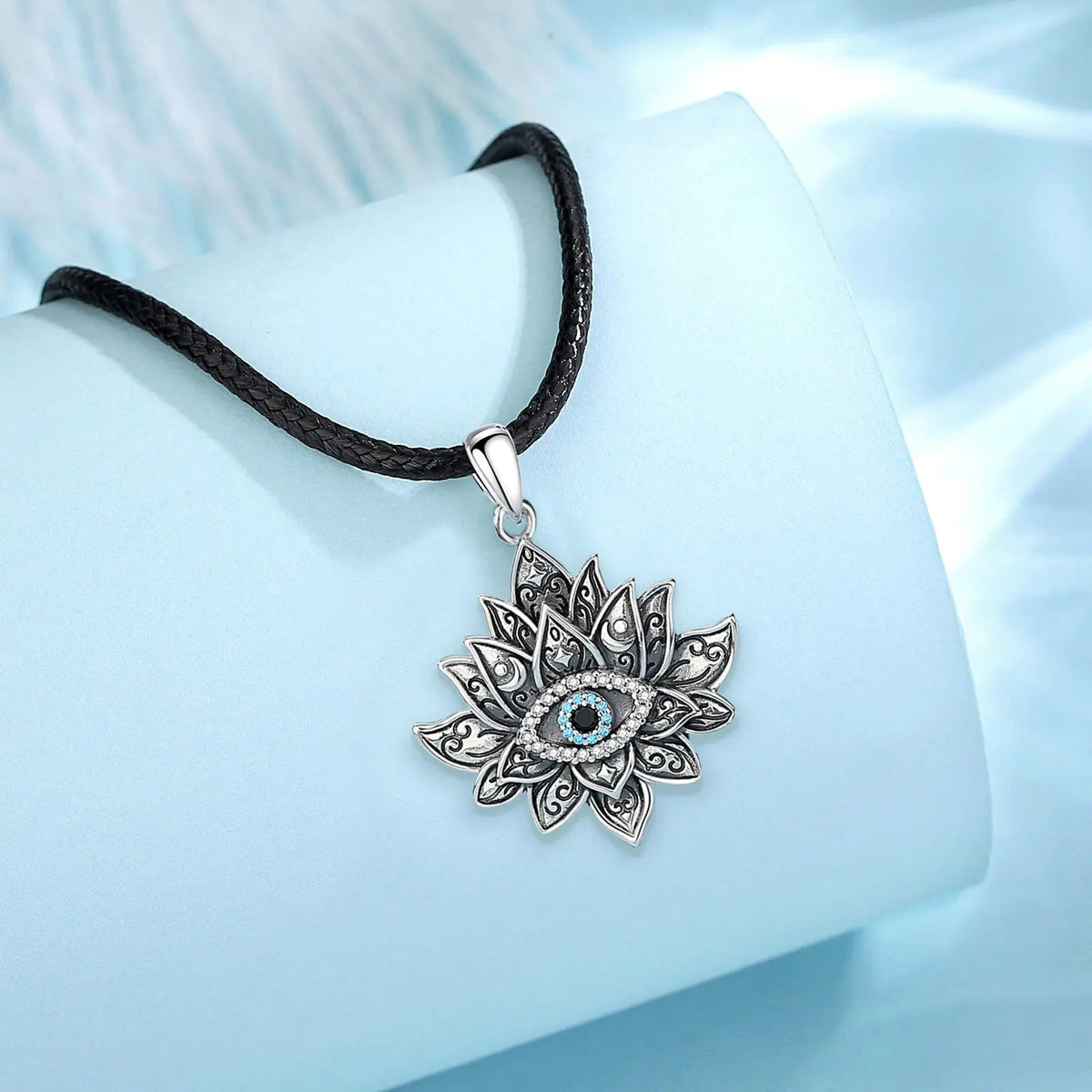 Lotus evil eye pendant displayed on a black braided rope against pale blue fabric
